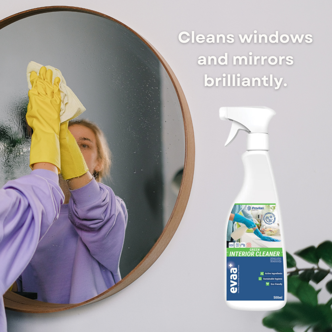 Person cleaning a mirror. A spray bottle of Provilan Evaa Probiotic Green Interior Cleaner is in the foreground, alongside text saying "Cleans windows and mirrors brilliantly".