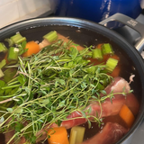 Greens, celery, carrots and raw bones in a pot while bone broth is being made.