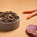 A bowl of DARF Cold Pressed Light dog food beside raw beef and carrots.