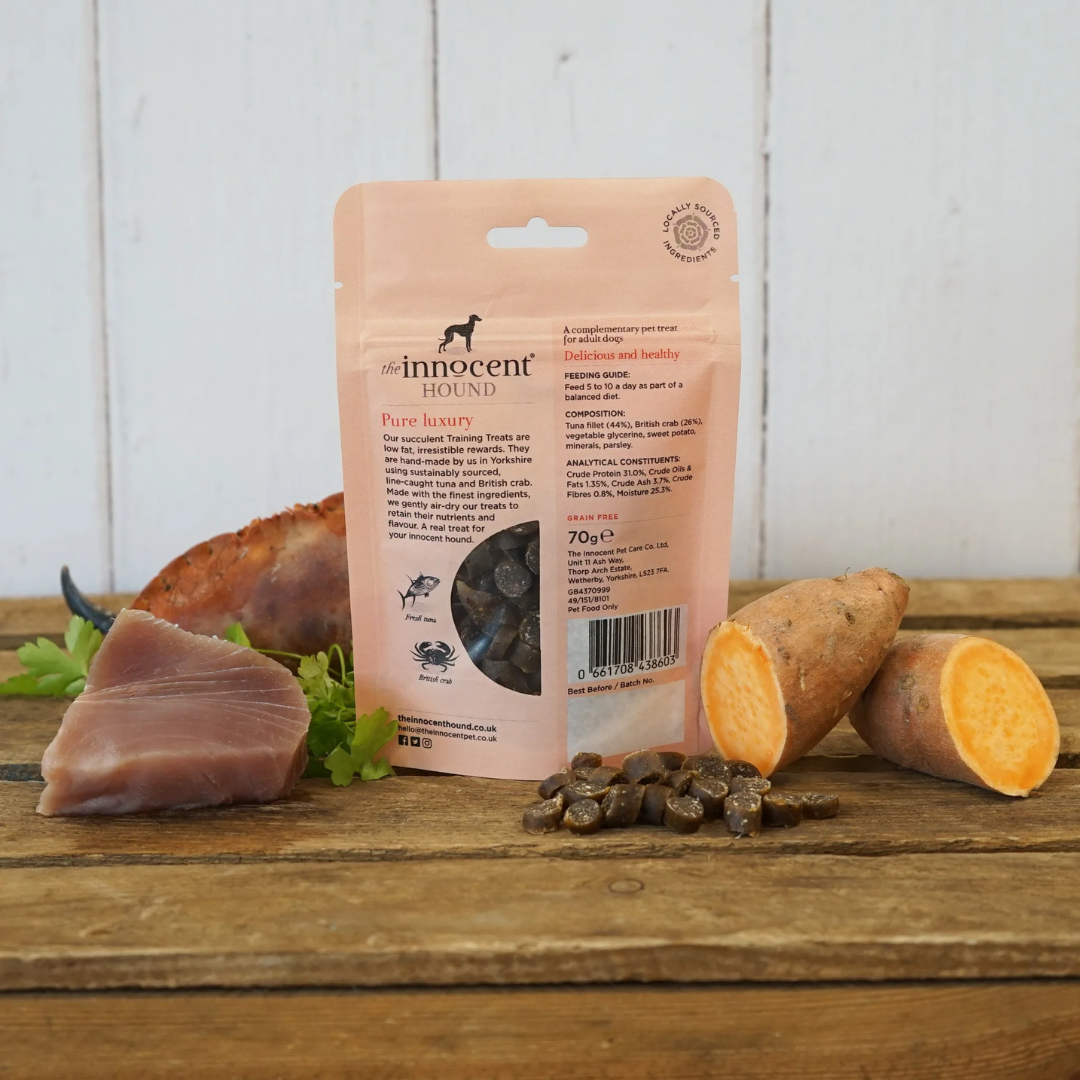 Back of a Bag of Innocent Hound Training Treats Tuna and Crab Rewards on a wooden surface, surrounded by raw ingredients and loose treats.